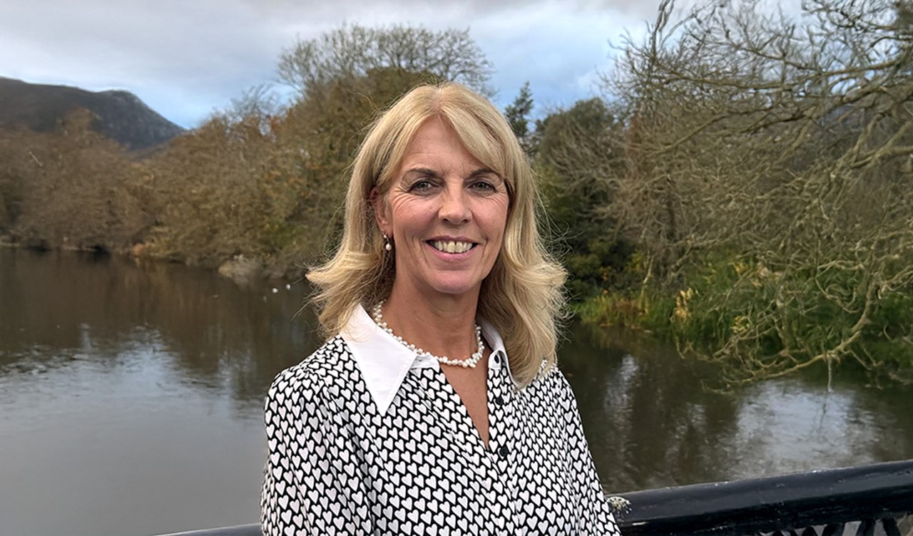 Close up of a woman standing on a bridge with a river and countryside in the background